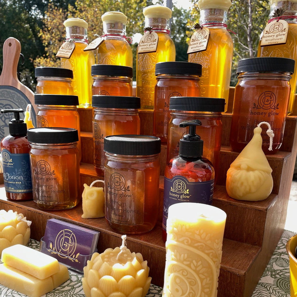 Collection of amber-colored bottles with black caps filled with honey on a wooden stand, surrounded by decorative items.