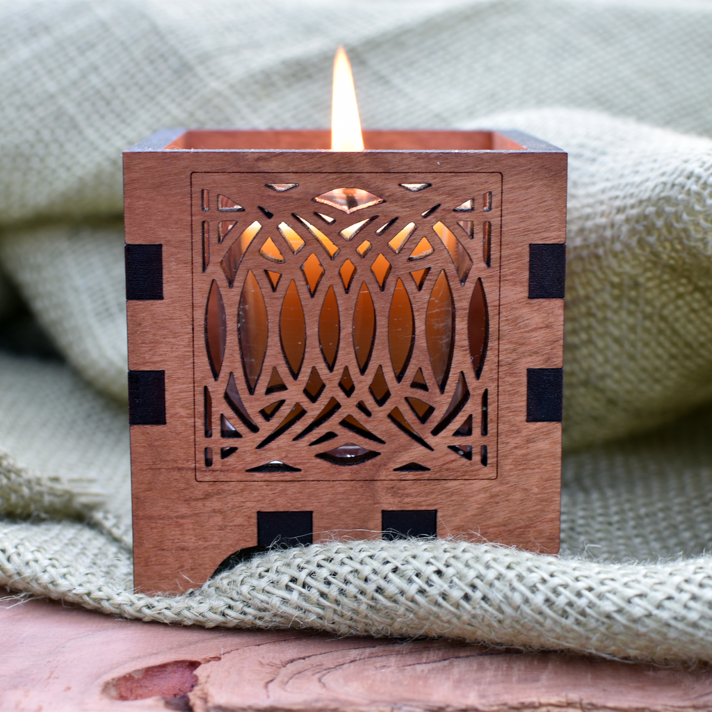 A brown tea light candle holder with a swirl design, made from cherry wood, displayed with a lit candle inside, placed on a burlap fabric.
